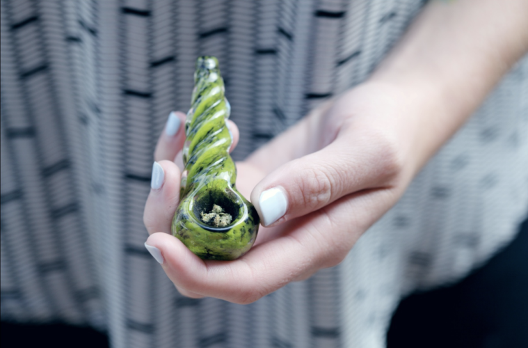 A woman’s hand holding a glass pipe with marijuana in it
