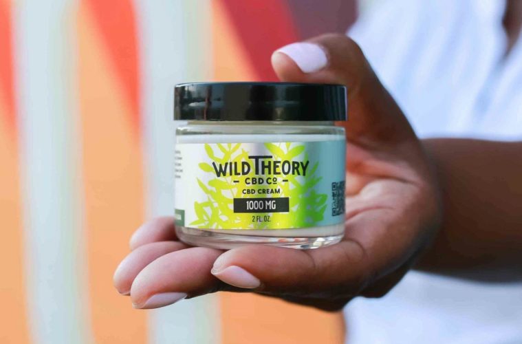 Hand holding one Wild Theory Cream inside of glass jar with black top.